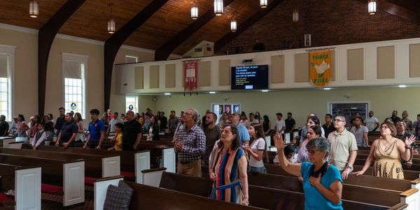 Congregation engaged in worship inside a church with wooden ceiling and banners.