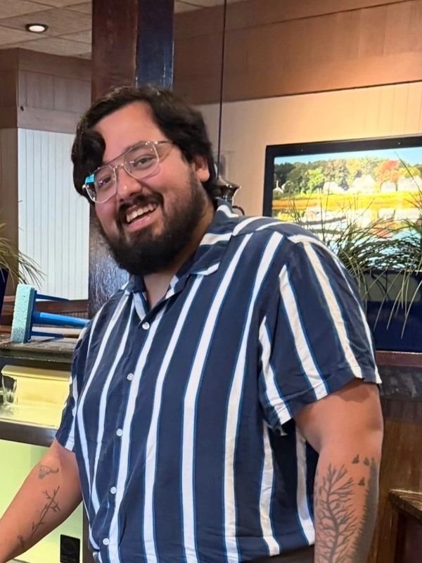 Smiling man with glasses and tattoos wearing a striped shirt.