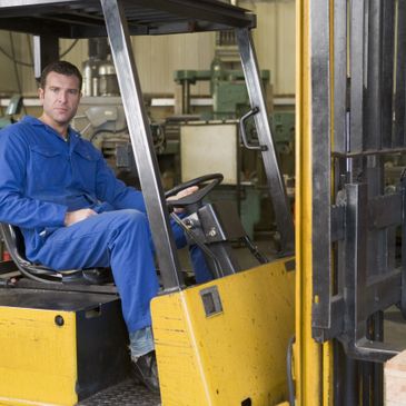 Worker in blue coveralls operating a yellow forklift in a factory.