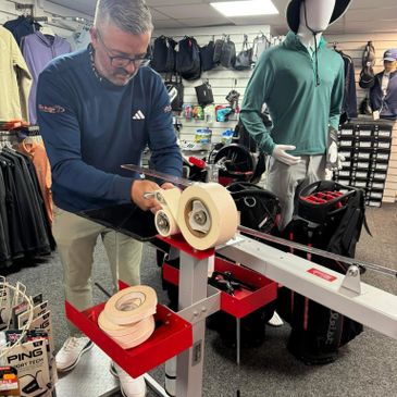 Man adjusting a golf club using a specialized fitting machine in a golf shop.