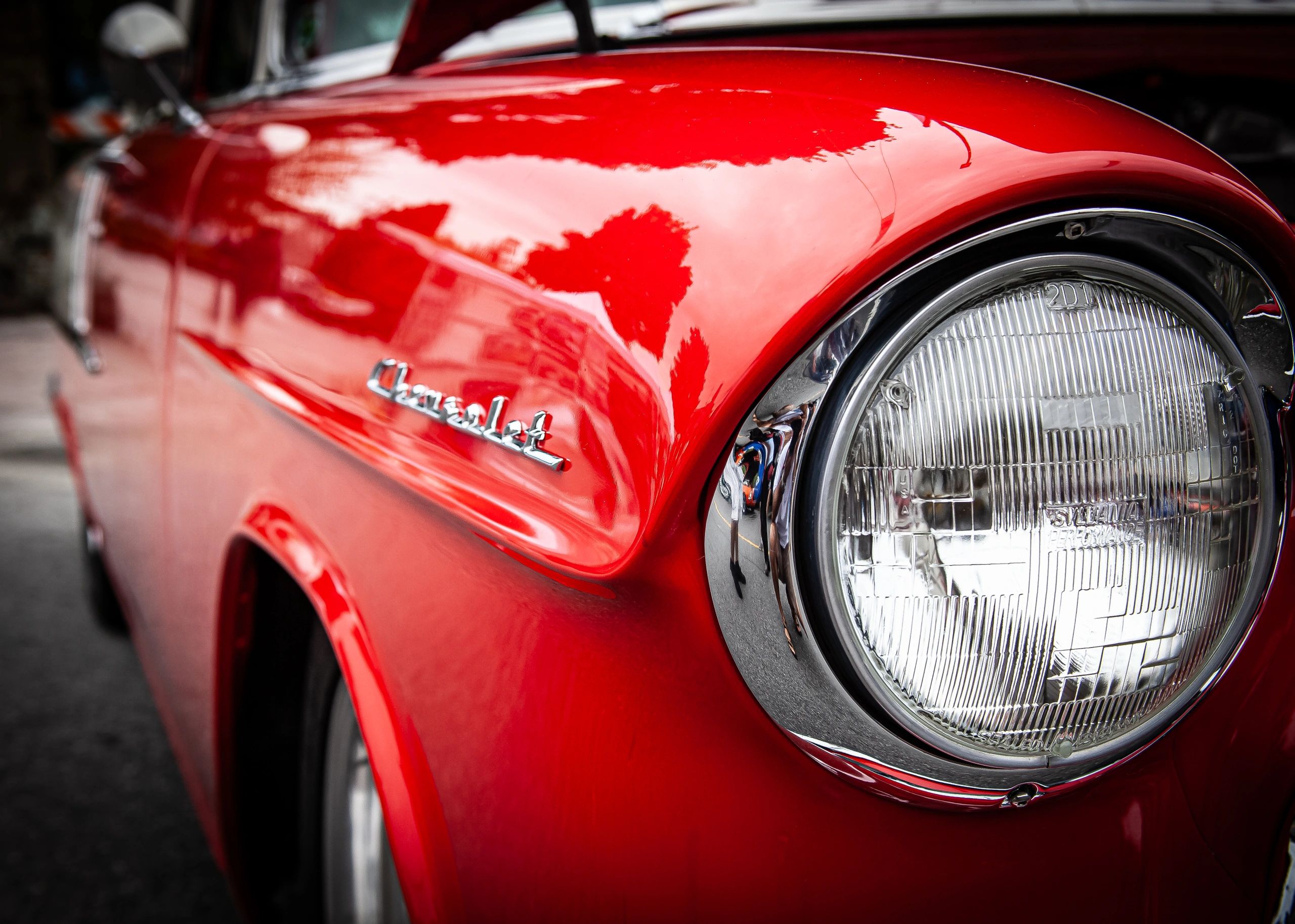 Close-up of a shiny red Chevrolet car headlight and fender.