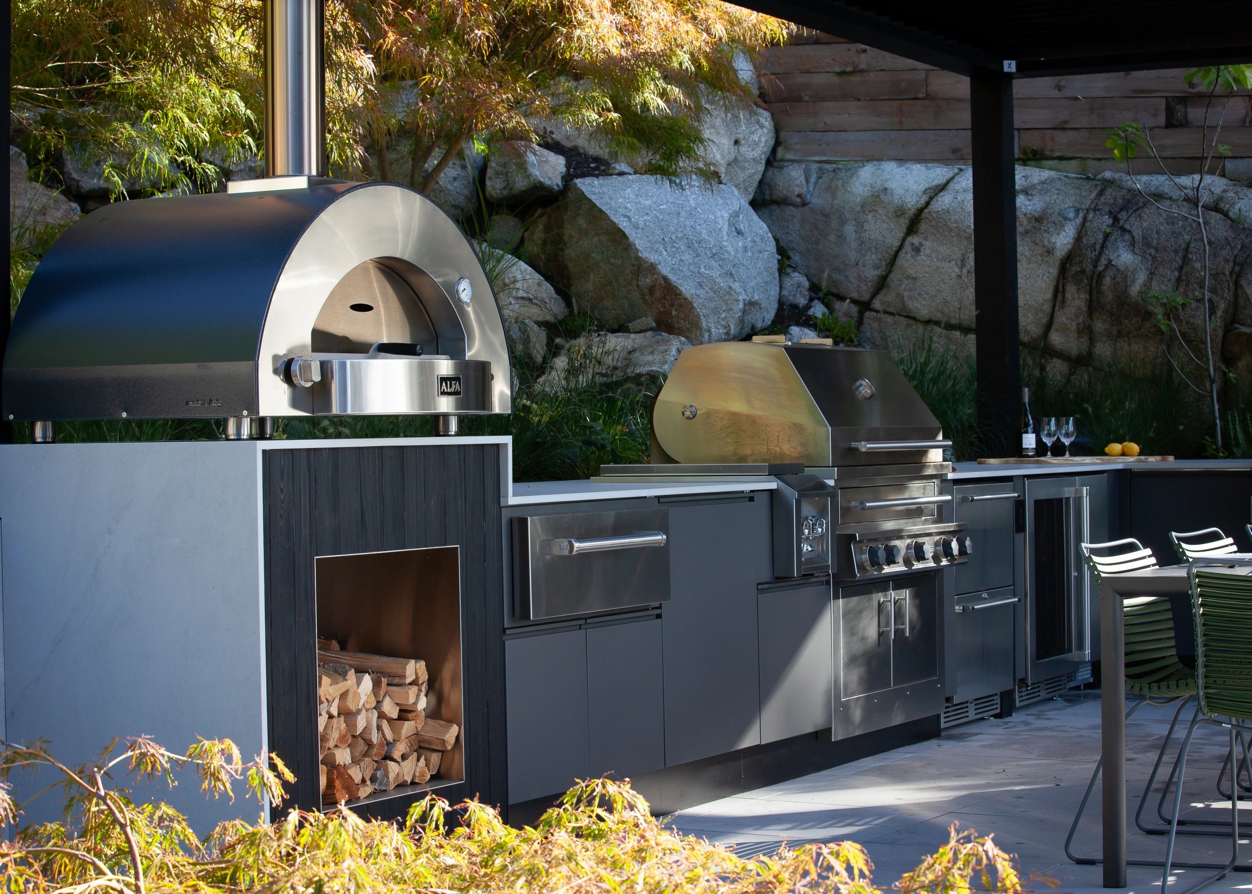 Modern outdoor kitchen with pizza oven and grill under a covered patio.