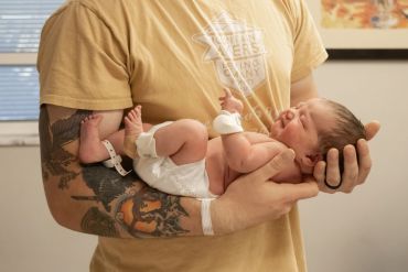 Man holding a newborn baby with tattoos on his arm.