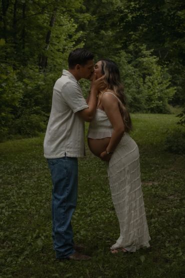 Couple sharing a kiss in a forest, woman is pregnant.