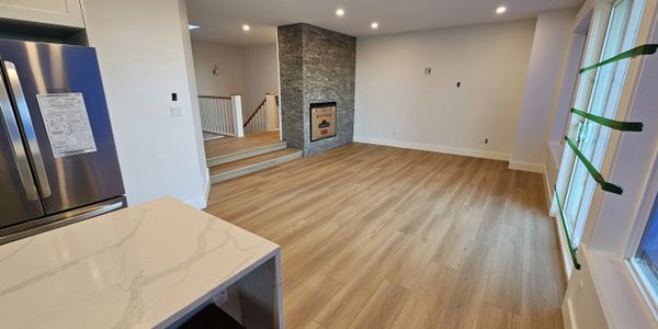 Modern empty living room with light wood flooring and stone fireplace.