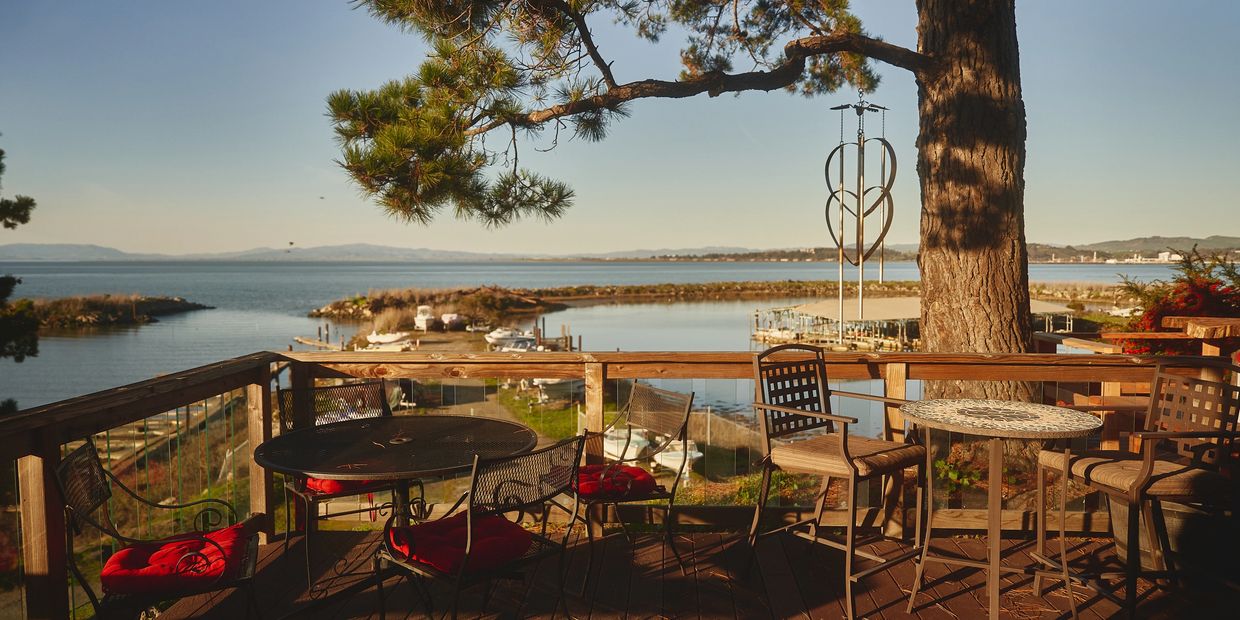 View of a sunset from the deck with a large tree and table and chairs with a heart shaped wind chime.