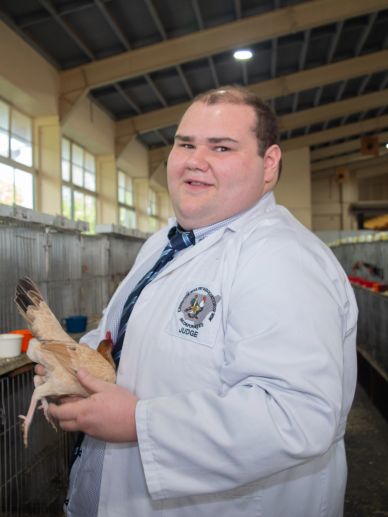Man in white coat holding a chicken inside a poultry facility.