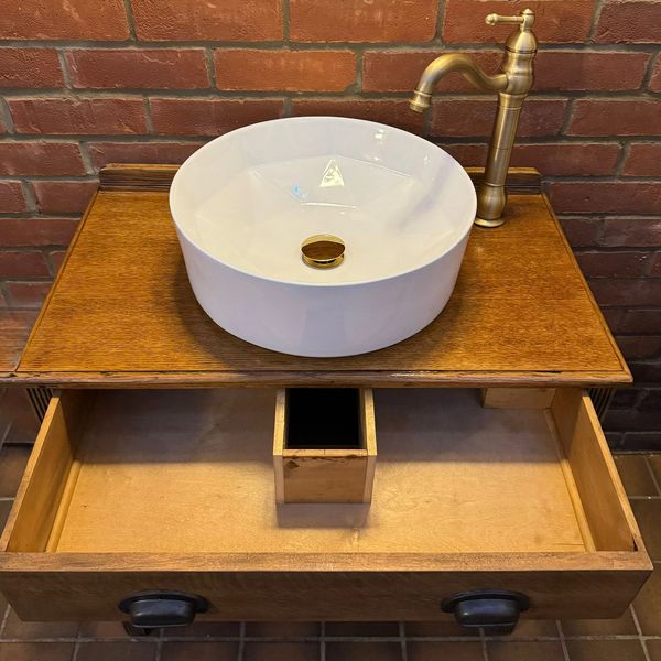 White circular ceramic basin with brass effect tap with drawer converted for plumbing.