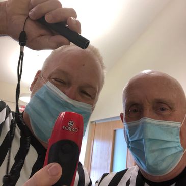 Two men in referees' uniforms wearing masks, holding a red device.