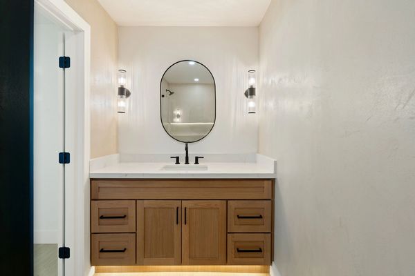 White oak bathroom vanity. Black oval mirror. Black designer sconces next to vanity mirror. White oa