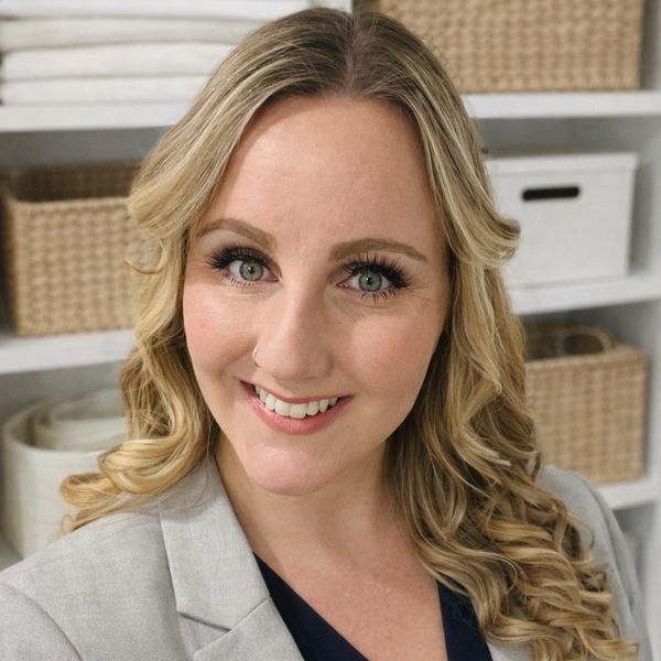 Smiling woman with curly blonde hair in a gray blazer indoors.