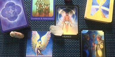 A spread of tarot and oracle cards with crystals on a woven mat.