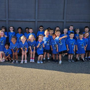 Group of young children wearing matching blue shirts posing outdoors.