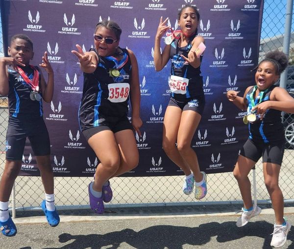 Four young athletes joyfully jump with medals at a USATF Pacific Northwest event.