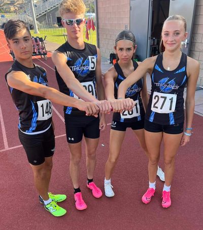 Four young athletes in matching uniforms join hands on a running track.
