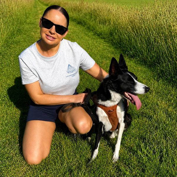 Woman in sunglasses kneeling on grass with her black and white dog.