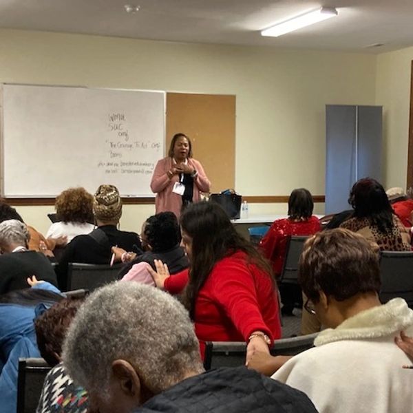 Woman speaking to a seated audience in a classroom setting.