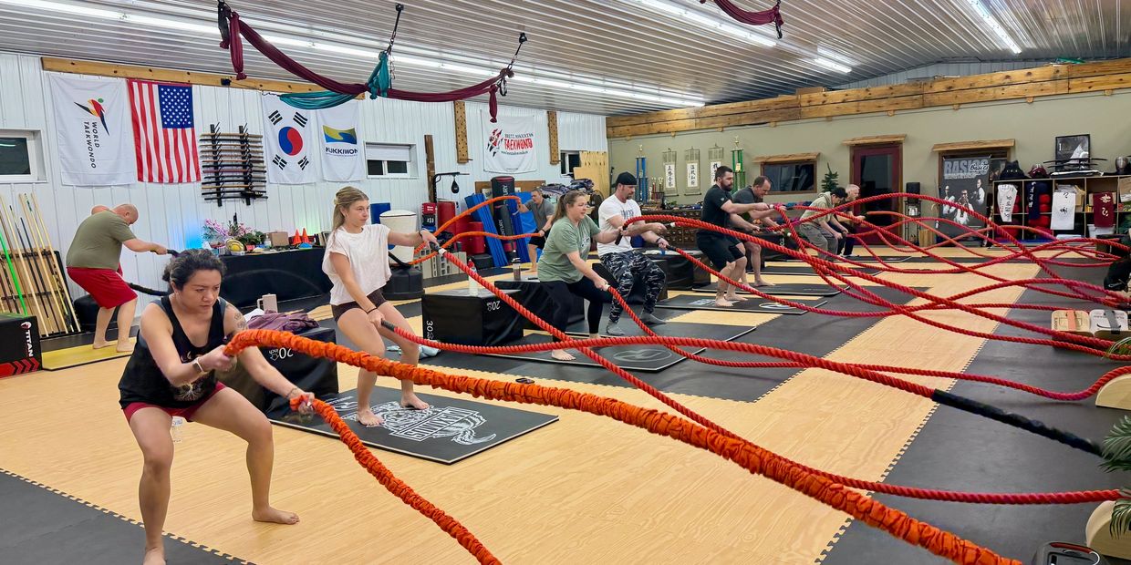 Group exercise class using battle ropes in a martial arts gym.