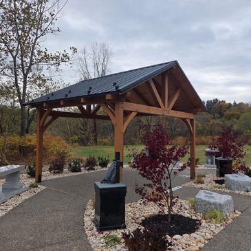 A wooden pavilion in a landscaped garden area with stone benches and plants.