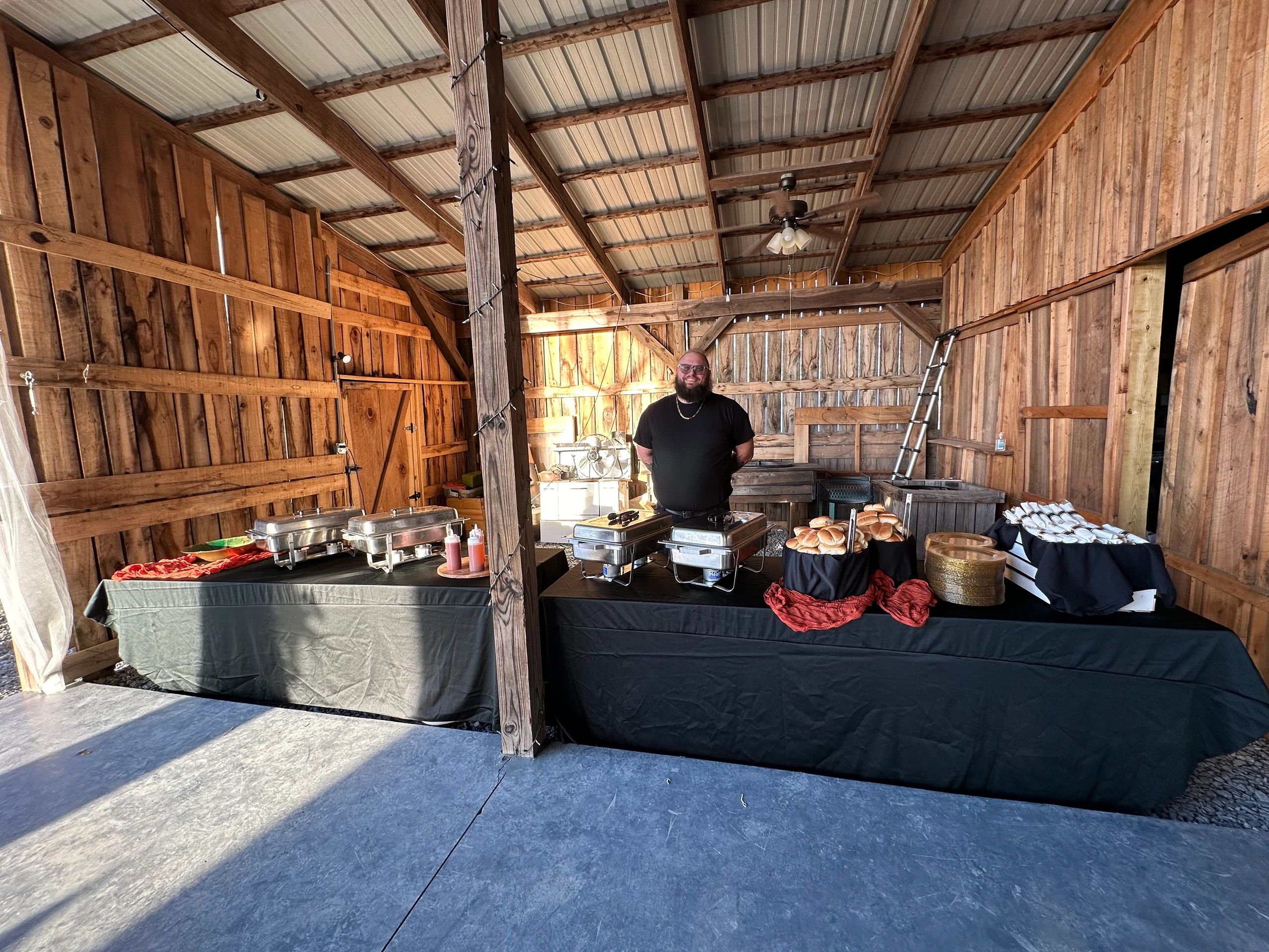 Man standing behind a buffet setup in a wooden barn.