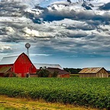 Red barn and windmill under a dramatic cloudy sky on a farm.
