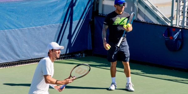 Dos hombres juegan tenis en una cancha al aire libre.