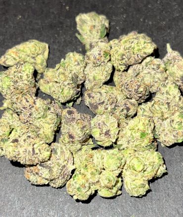 Close-up of green and purple cannabis buds on a dark surface.