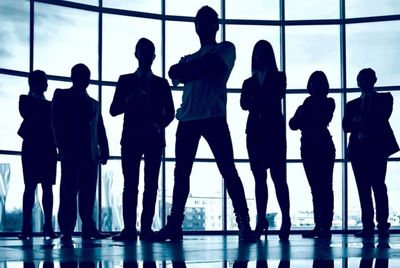Silhouetted group of business professionals standing confidently in front of large windows.