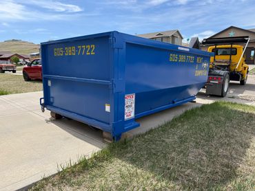 Large blue dumpster with contact number parked near a driveway.