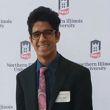 Yousuf Khan posing in a suit and tie in front of a NIU banner