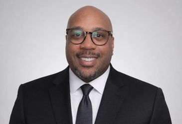 Smiling man in glasses and a black suit with a tie.