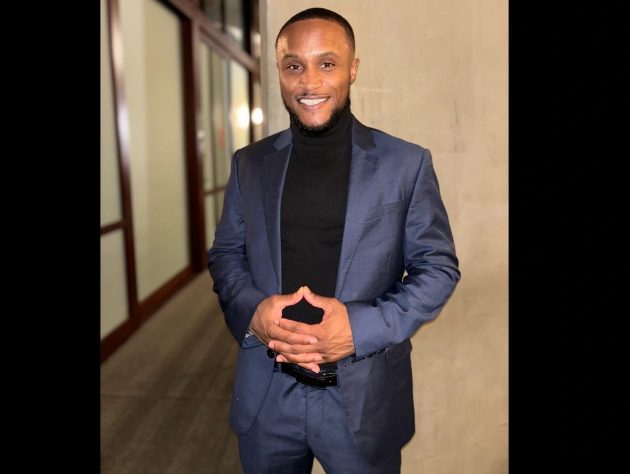 Man standing with warm smile wearing a navy suit with black turtleneck
