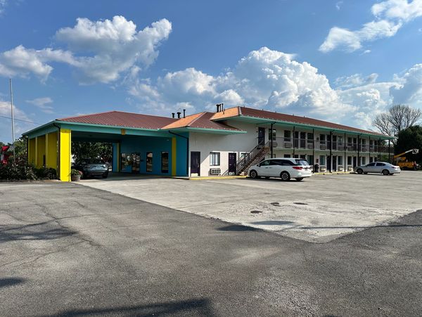 Two-story motel with bright yellow and blue entrance under a partly cloudy sky.