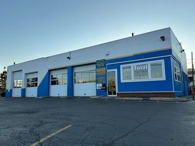 A white and blue auto repair shop with garage doors and a parking lot.