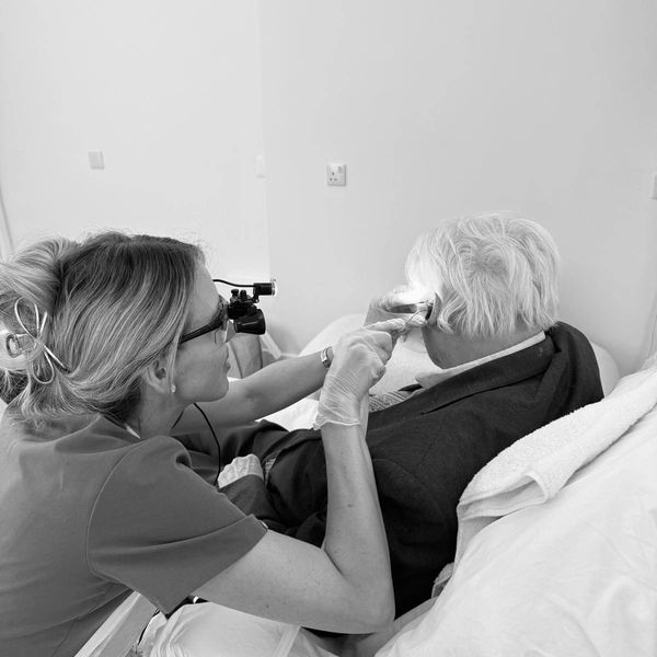 Healthcare professional examines elderly man's ear using specialized equipment.