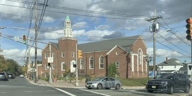 Brick church under a cloudy sky at an intersection with cars waiting at a traffic light.