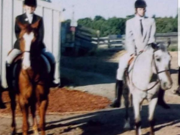 Two riders on horses in an outdoor arena.