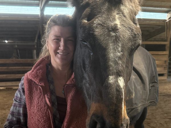 Woman smiling beside a horse in a barn.