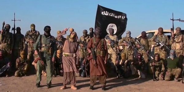 Group of armed militants posing with a black flag under clear sky.