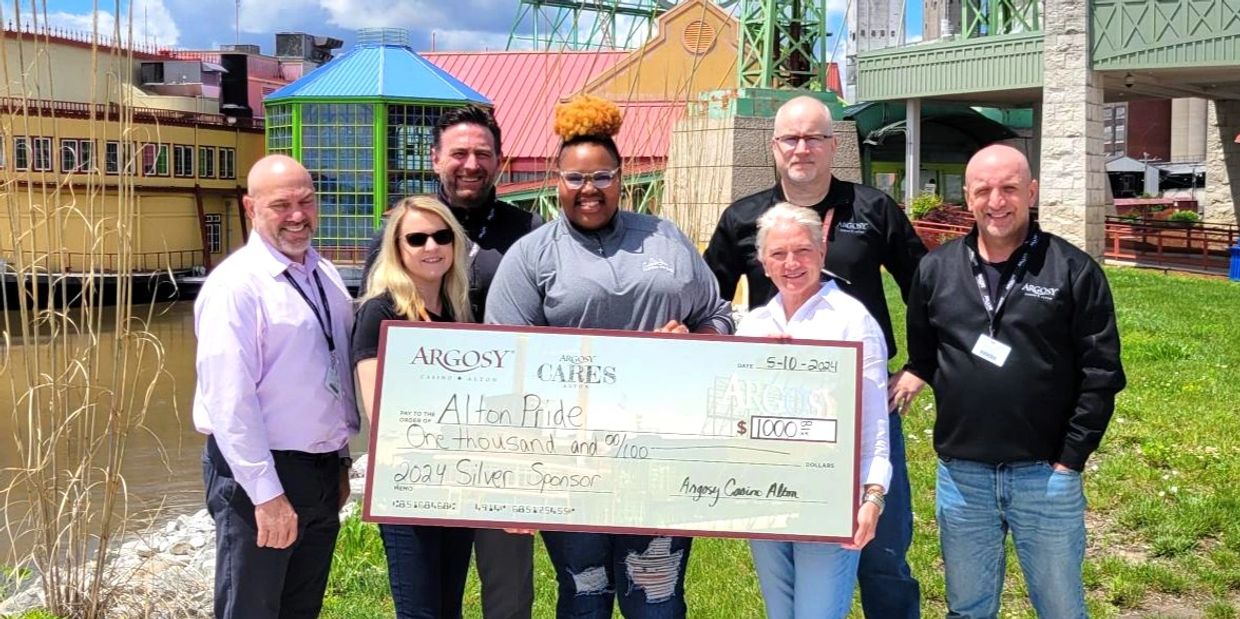 Group of seven people holding a large $1000 donation check outdoors.