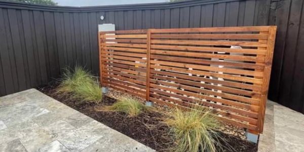 Modern wooden slatted fence with plants in a minimalist backyard corner.
