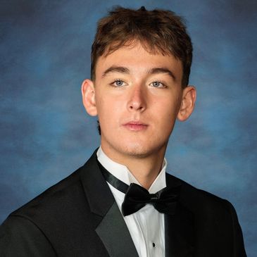 Young man in a tuxedo against a blue backdrop.