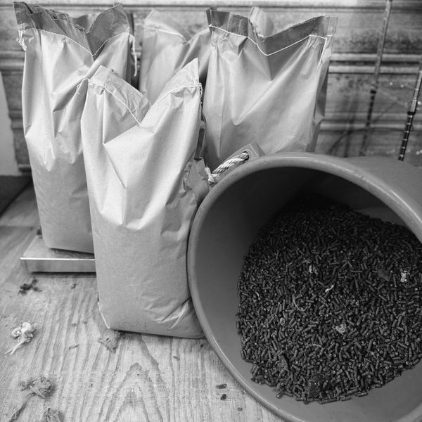 Bags and a bucket filled with pellets on a wooden floor.