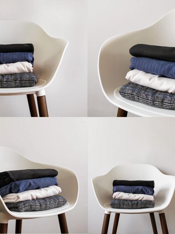 Stack of folded clothes on a white chair with wooden legs.