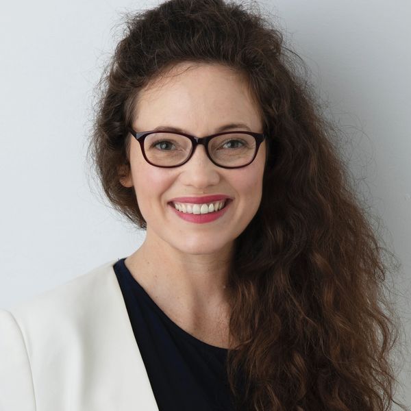 Smiling woman with glasses and long curly hair.