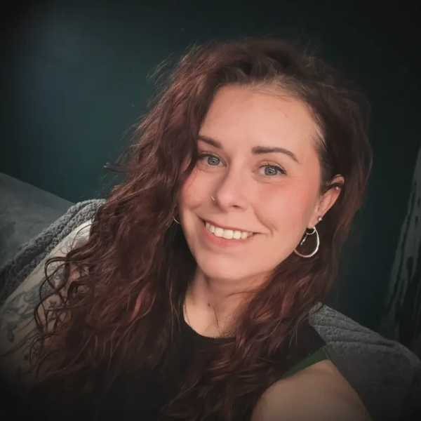Smiling woman with curly auburn hair and hoop earrings.