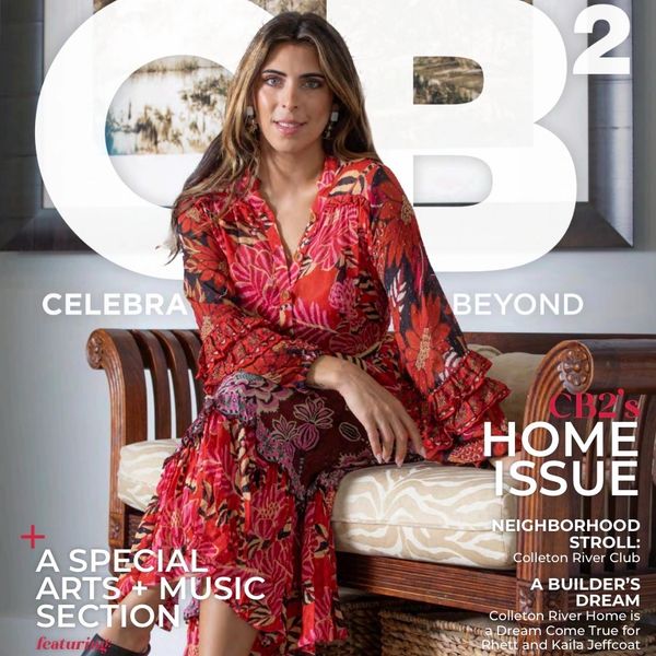 Woman in a vibrant floral dress poses on a wooden bench for a magazine cover.