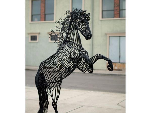 A black metal sculpture of a rearing horse on a sidewalk.
