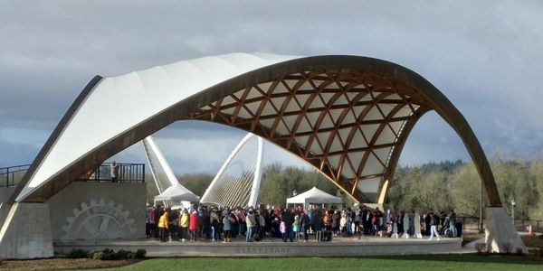 Crowd gathered under a modern curved pavilion with a wooden lattice roof.