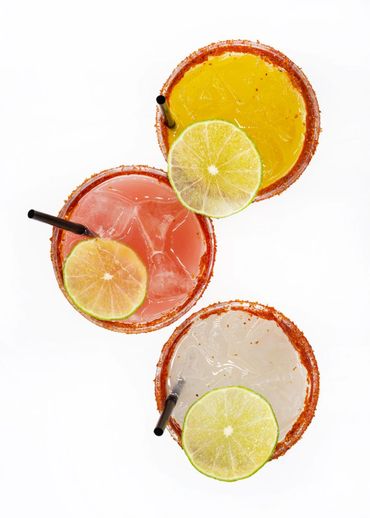 Three colorful cocktails with lime slices and salted rims.